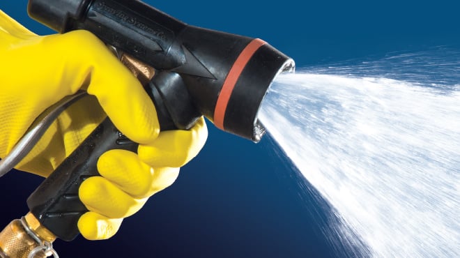 hand in yellow rubber glove holding a GunJet spraying water