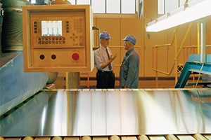 two men talking in a steel mill next to a conveyor