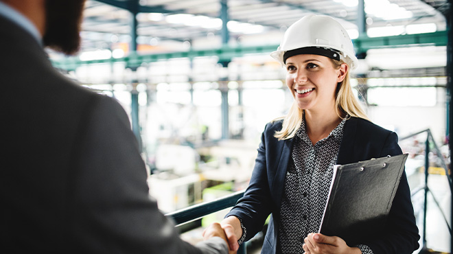 women in hard hat holding clipboard shaking hands