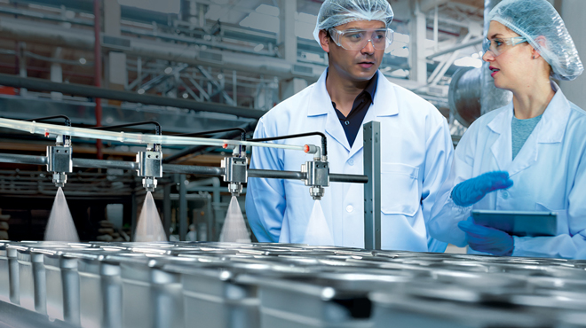 employees in hair nets standing at conveyor with bread pans being sprayed