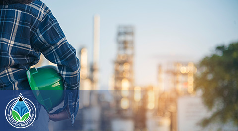 back view of person holding hard hat looking at a chemical plant